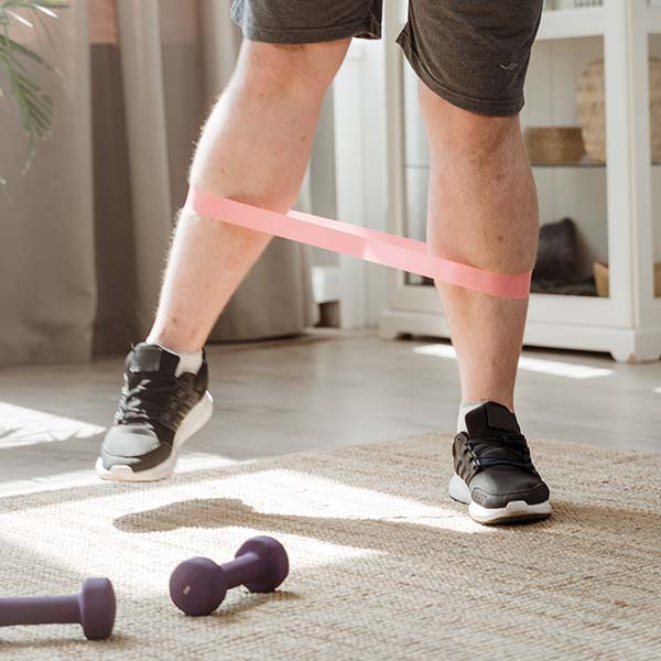 Foto van de benen van een persoon die traint met een oefenband en gewichten